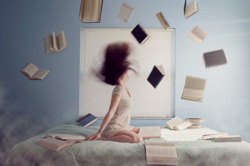 Kobieta siedząca na łóżku. Dookoła książki, notesy, telefony.